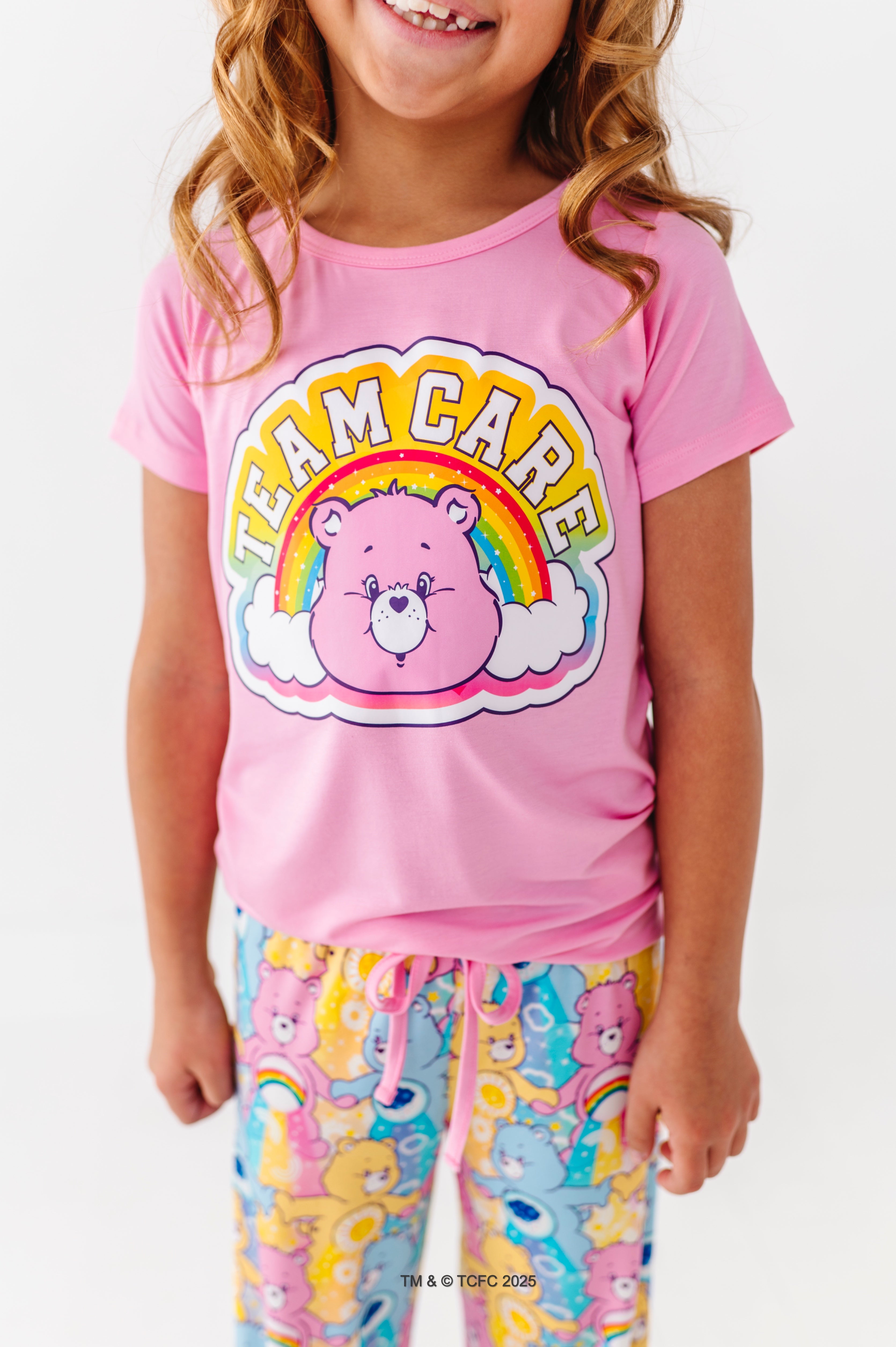 Child wearing pink Care Bears™ “Team Care” t-shirt with rainbow graphic and matching Care Bears print lounge pants